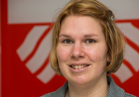 Eine Person mit unkenntlich gemachtem Gesicht vor einem rot-weißen Hintergrund mit einem Design oder Logo.