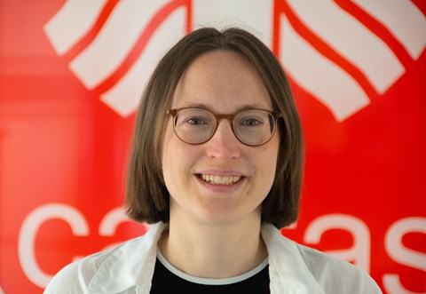 Eine Person mit kurzen braunen Haaren, einem weißen Hemd über einem schwarzen Oberteil.